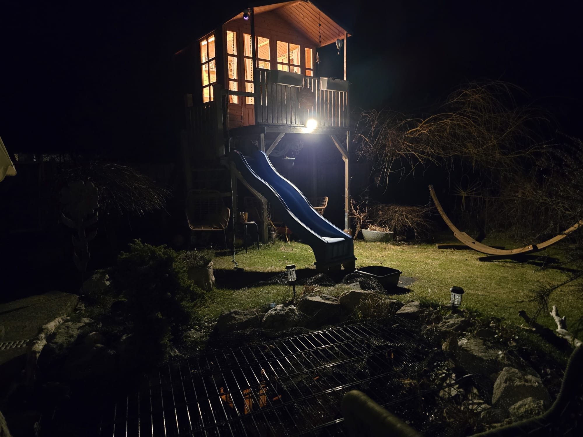Beleuchteter Gartenbereich bei Nacht mit Gartenhaus und Wegen